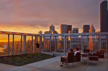 Two people sitting on a rooftop terrace overlooking a city skyline at sunset.